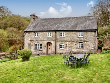 A stone cottage with a wooden door and white windows and a metal outdoor dining table with chairs on grass at The Birches in Hay-on-Wye