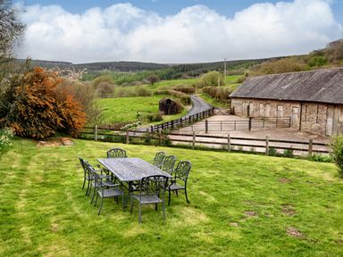 An outdoor dining table with six chairs on a grassy area near a barn and a road at The Birches in Hay-on-Wye