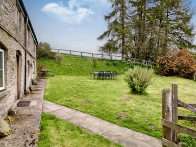 A grassy garden with a stone path and outdoor table and chairs near a stone house at The Birches in Hay-on-Wye