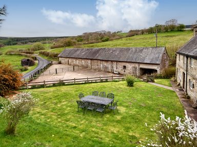 An outdoor metal table with eight chairs on grassy lawn next to stone buildings and a fenced yard at The Birches in Hay-on-Wye
