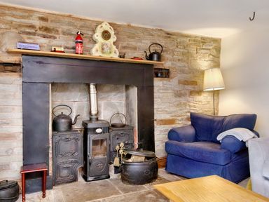 A sitting area with a blue armchair a floor lamp and a fireplace with a wood stove at The Birches in Hay-on-Wye