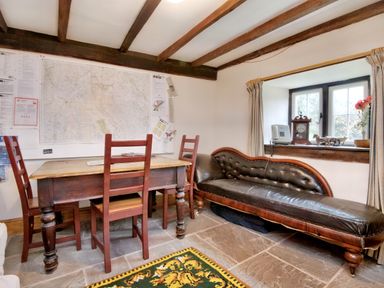 A room with a wooden table and three chairs a leather chaise lounge under a window with curtains and a wall map at The Birches in Hay-on-Wye