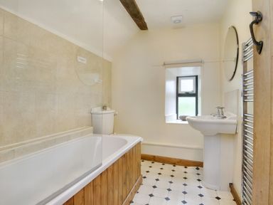 A bathroom with a bathtub a toilet a sink a round mirror a window and a heated towel rail at The Birches in Hay-on-Wye