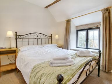 A bedroom with a metal bed frame two bedside tables with lamps towels on a bed and a window with curtains at The Birches in Hay-on-Wye