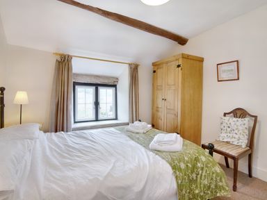 A bedroom with a bed towels on a green blanket a wooden wardrobe a chair and a window at The Birches in Hay-on-Wye
