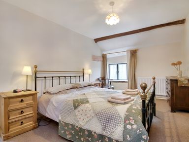 A bedroom with a double bed covered with a quilt and towels on it two bedside tables with lamps and a dresser with flowers at The Birches in Hay-on-Wye