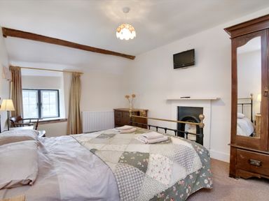 A bedroom with a bed covered by a patchwork quilt two folded towels a wooden chair a wooden dresser a wall-mounted television a fireplace and a wooden wardrobe with a mirror at The Birches in Hay-on-Wye