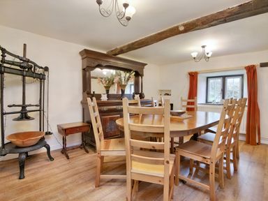 A dining room with a wooden table and chairs a wooden sideboard and window with orange curtains at The Birches in Hay-on-Wye