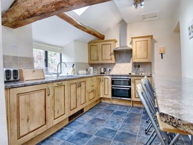 A kitchen with wooden cabinets a tiled floor and a breakfast bar with chairs at The Birches in Hay-on-Wye