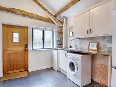 A utility room with wooden door washing machine sink and white cabinets at The Birches in Hay-on-Wye