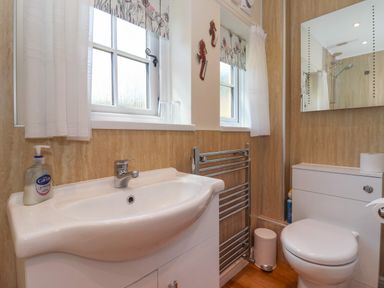 A bathroom with a sink, toilet, towel rack, two windows, and a mirror at Waggoner's Cottage in Bessingby near Bridlington