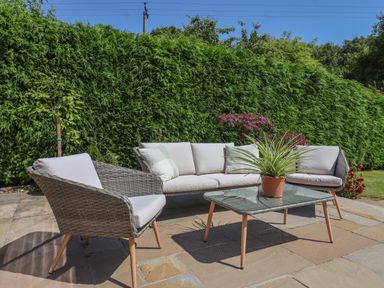 An outdoor patio with a wicker sofa, armchair, glass coffee table, and potted plant at Waggoner's Cottage in Bessingby near Bridlington