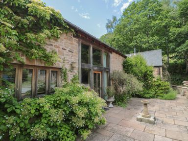 An outdoor view of a stone building with windows and plants at The Lodge Farm Barn in Deepdean near Ross-on-Wye