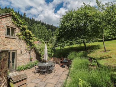 A garden with a stone patio, table, chairs, and trees at The Lodge Farm Barn Deepdean near Ross-on-Wye