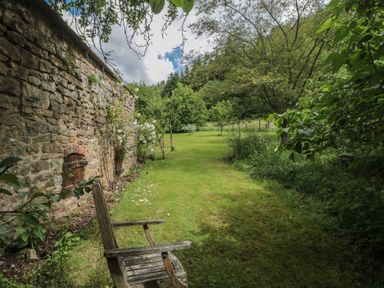 A garden with a stone wall and a wooden chair at The Lodge Farm Barn Deepdean near Ross-on-Wye