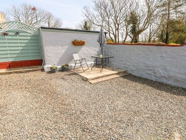 An outdoor gravel patio area with two chairs a table with an umbrella and flower pots on the wall at Ffynnon Tom in Trefin near St Davids