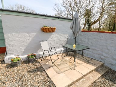 A small patio area with two chairs a table with an umbrella and potted plants at Ffynnon Tom in Trefin near St Davids