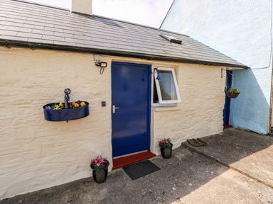 The exterior of a stone building with a blue door and flower pots at Ffynnon Tom in Trefin near St Davids