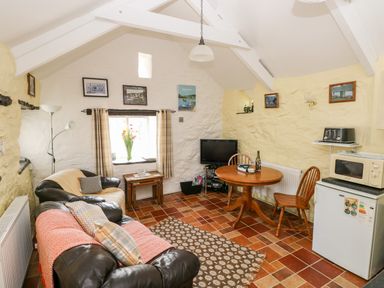 A living room with leather sofas a wooden round table a television and kitchen appliances at Ffynnon Tom in Trefin near St Davids