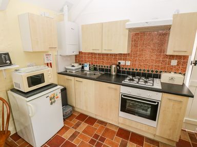 A kitchen with wooden cabinets a white oven a microwave a toaster a kettle and a bread box at Ffynnon Tom in Trefin near St Davids