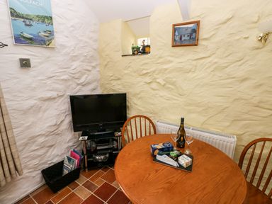 A dining area with a round wooden table and two chairs next to a TV on a stand against textured walls at Ffynnon Tom in Trefin near St Davids