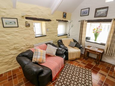A sitting room with two black armchairs a small wooden table with flowers on it and framed pictures on white and yellow walls at Ffynnon Tom in Trefin near St Davids