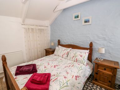 A bedroom with a wooden double bed floral bedding and two bedside tables with lamps at Ffynnon Tom in Trefin near St Davids