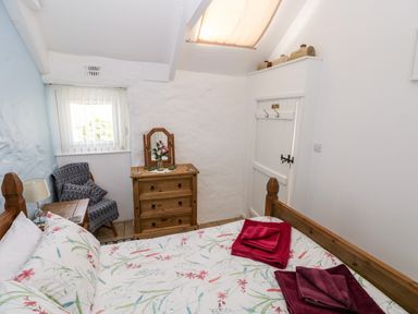 A bedroom with a wooden bed floral bedding wooden chest of drawers armchair and a small window at Ffynnon Tom in Trefin near St Davids