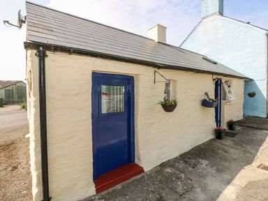 Exterior of a small stone cottage with blue doors and hanging flower baskets at Ffynnon Tom in Trefin near St Davids