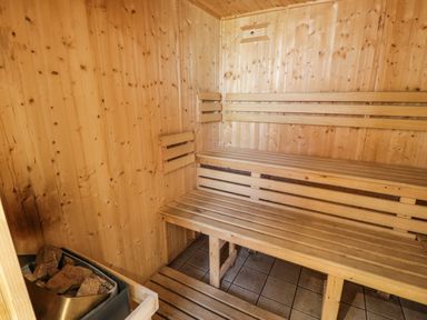 An interior of a wooden sauna with benches and a heater with stones at Halford Hill in Llanberis