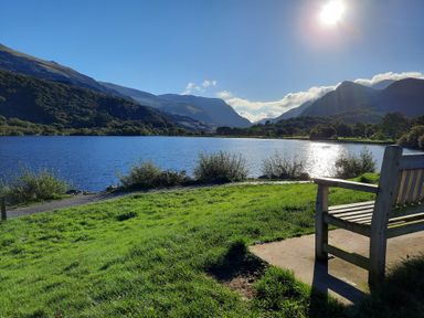 A lakeside view with a wooden bench on grass and mountains in the background at Halford Hill in Llanberis