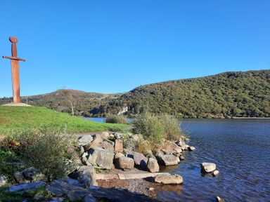 A lakeside view with a large sword sculpture on a grassy hill and hills in the background at Halford Hill in Llanberis