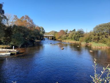 A river with rocks and trees on both sides and a bridge in the distance at Halford Hill in Llanberis