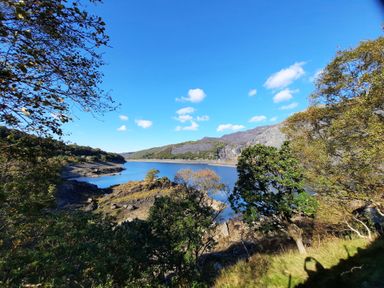 A lake surrounded by trees and hills under a blue sky at Halford Hill in Llanberis