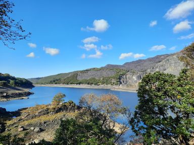 A view of a river or lake with rocky hills and trees under a blue sky at Halford Hill in Llanberis