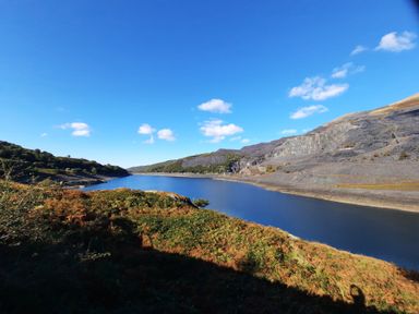 A river running between hills with vegetation and rocky slopes under a blue sky at Halford Hill in Llanberis