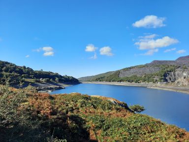 A river with hills and vegetation under a blue sky at Halford Hill in Llanberis