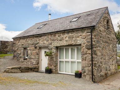A stone cottage with a white door and window with flower pots outside at Hendre Cottage Bronaber near Trawsfynydd