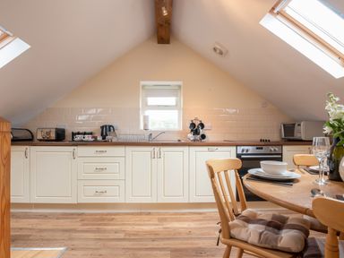 A kitchen with cream cabinets wooden countertops a dining table set with dishes glasses and flowers at Hendre Cottage Bronaber near Trawsfynydd