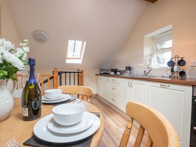 A kitchen with white cabinets wooden countertops a dining table with plates bowls a bottle and flowers at Hendre Cottage in Bronaber near Trawsfynydd