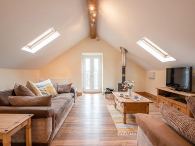 An attic living room with a sofa a coffee table a wood burner TV and skylight windows at Hendre Cottage Bronaber near Trawsfynydd