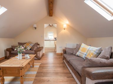 A living room with two brown sofas a wooden coffee table with flowers and cups and a view to a kitchen at Hendre Cottage in Bronaber near Trawsfynydd