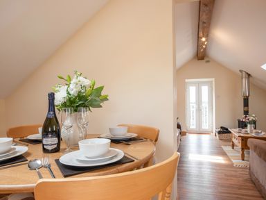 A dining table set with white dishes glasses and a bottle of prosecco next to a living area with a coffee table and stove at Hendre Cottage Bronaber near Trawsfynydd