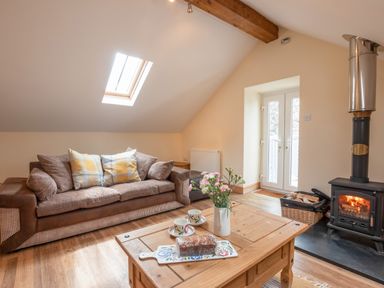 A living room with a sofa wooden coffee table with cake and flowers and a wood burning stove at Hendre Cottage in Bronaber near Trawsfynydd