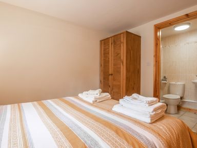 A bedroom with a bed, folded towels on the bed, a wooden wardrobe, and an open door showing a bathroom with a toilet and sink at Hendre Cottage in Bronaber near Trawsfynydd