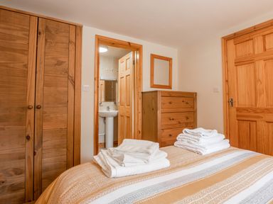 A bedroom with wooden wardrobe and dresser with mirror and towels on bed at Hendre Cottage in Bronaber near Trawsfynydd