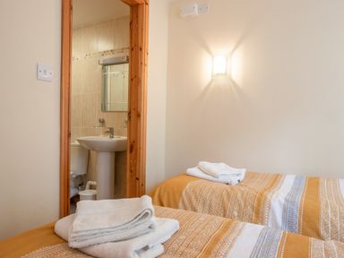A bedroom with two single beds with towels on them and an open door showing a bathroom with a sink and mirror at Hendre Cottage in Bronaber near Trawsfynydd