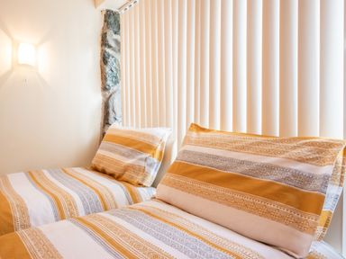 A bedroom with two single beds with patterned bedding next to a wall with cinderblock detail and vertical blinds at Hendre Cottage in Bronaber near Trawsfynydd