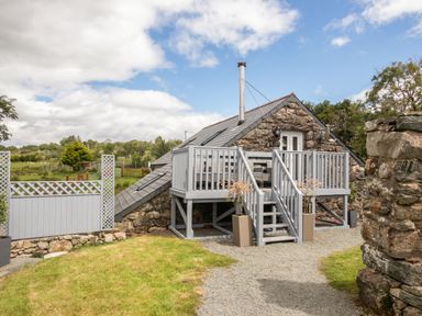 A stone cottage with a raised wooden deck and stairs leading to the door at Hendre Cottage Bronaber near Trawsfynydd