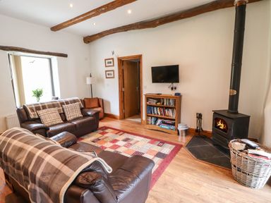 A living room with two leather sofas a wood burning stove and a bookshelf at The Hayloft in Newlands near Braithwaite and Keswick
